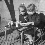 848108 Afbeelding van twee meisjes die een broodmaaltijd nuttigen aan een tafeltje op straat, vermoedelijk in Amsterdam-West.